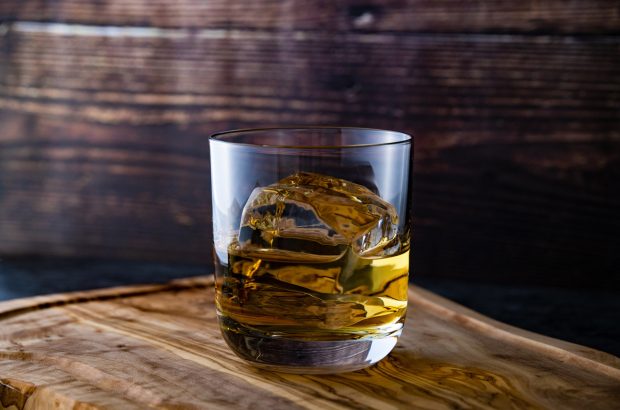 A glass of bourbon with ice on top of a barrel